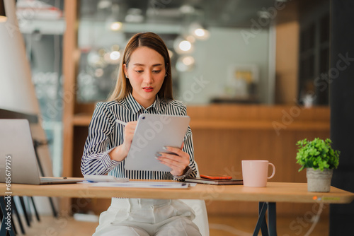 Cute Asian girl working on computer while consulting invoices and documents  calculator on table Planning to analyze financial reports business plan investment financial analysis concepts