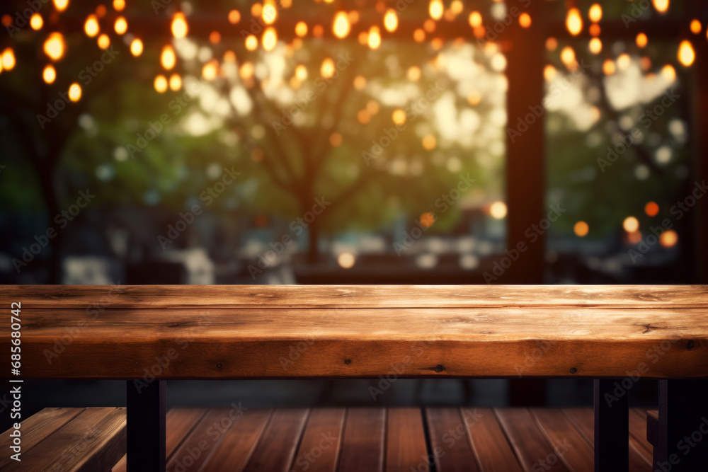An empty wooden table with a soft focus on blurred bokeh lights hanging from the trees in the background. Cozy evening at cafe concept