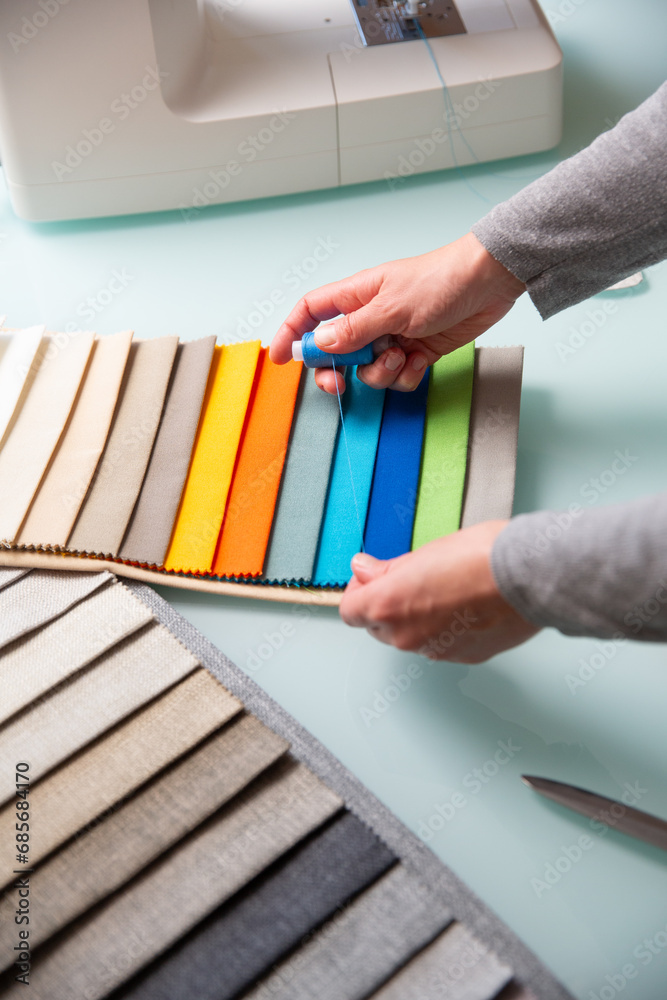 Obraz premium Tailor choosing right color of a blue thread using fabric samples on table during sewing process