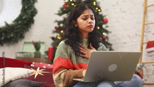 Charming young woman typing on laptop while get notification email and feeling upset reading bad negative news message before holidays sitting near Christmas tree at home Disappointment concept photo