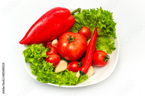 Mix of fresh vegetables - bell peppers and chilies, garlic, tomatoes, green salad in a white bowl.