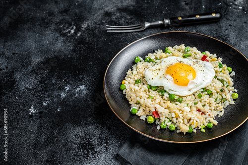 Fried rice with chicken, egg and vegetables in a plate. Black background. Top view. Copy space