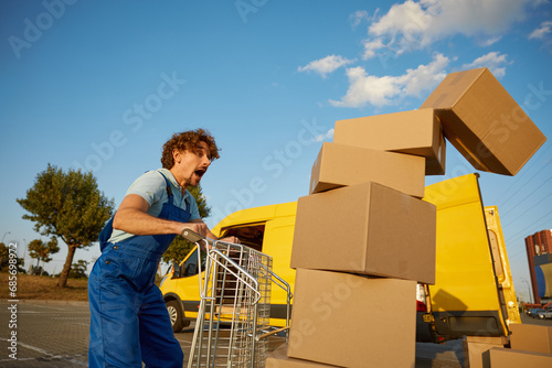 Foto Stressed courier screaming looking at falling parcel boxes from trolley cart