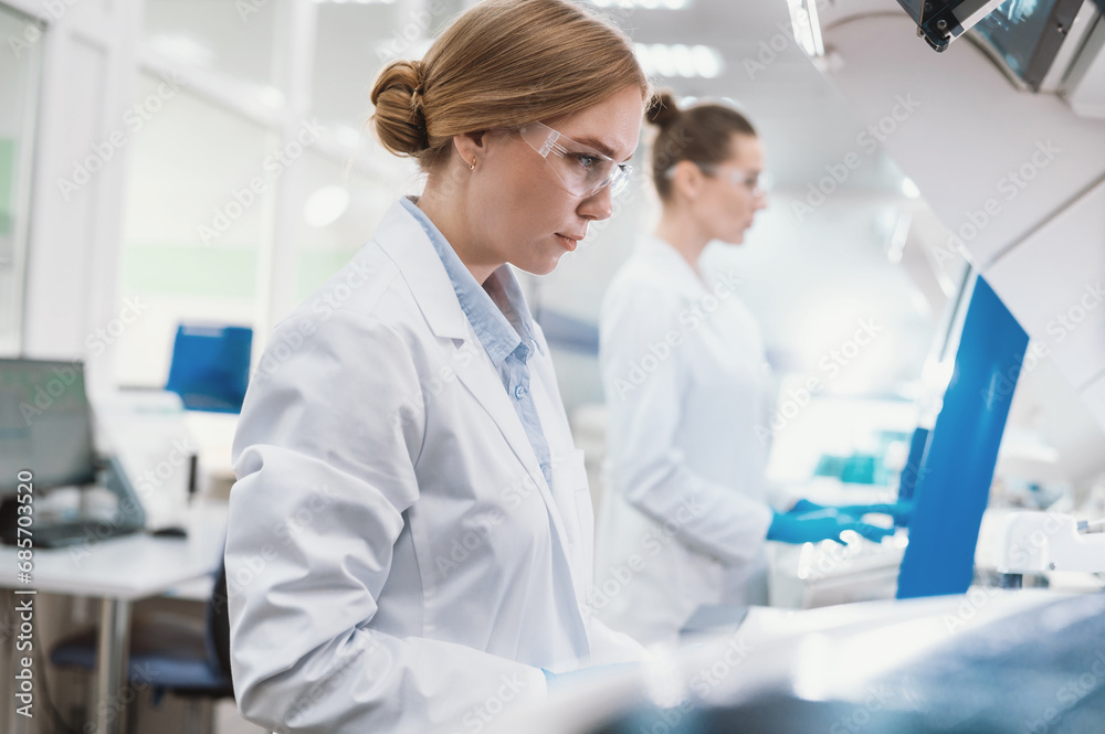 A team of laboratory technicians conduct a series of tests on a chemical analyzer in a biological laboratory. Two female scientists work in a modern equipped computer laboratory A team of laboratory technicians conduct a series of tests on a chemical analyzer in a biological laboratory. Two female scientists work in a modern equipped computer laboratory