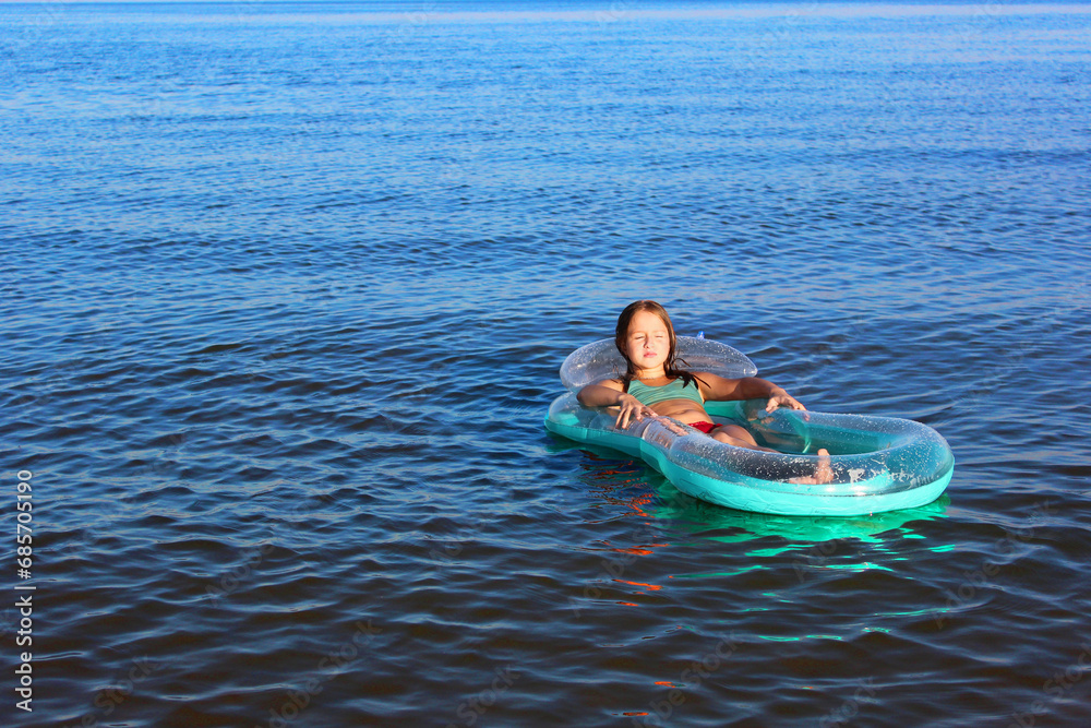 little happy girl in the sea with blond hair in a swimsuit floating in the sea on an inflatable blue mattress, Beautiful sunny seascape. the girl looks into the distance floats on calm water on the ho