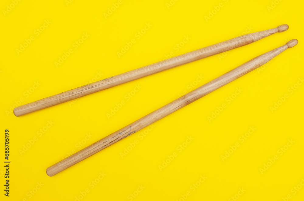 Two wooden drum sticks close up on yellow background Two wooden drum sticks close up on yellow background