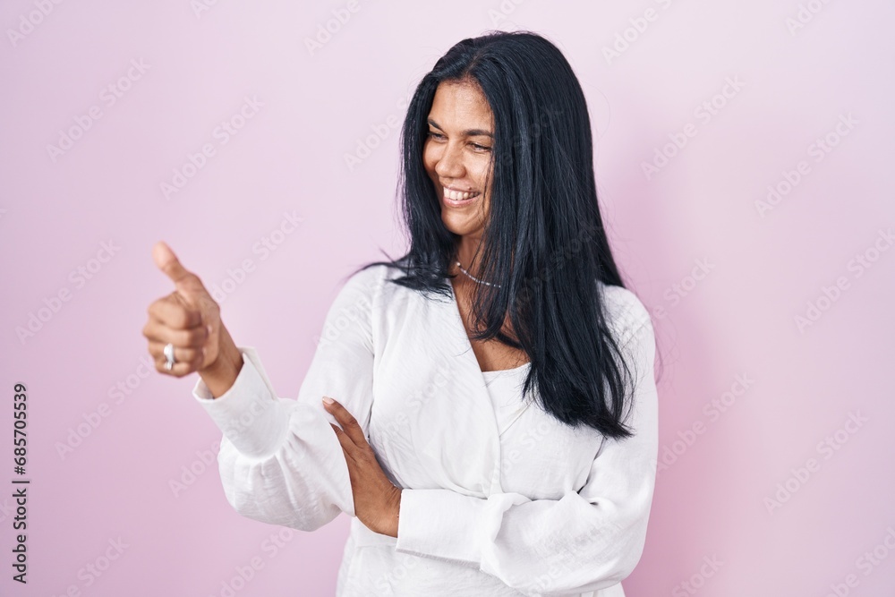 Mature hispanic woman standing over pink background looking proud, smiling doing thumbs up gesture to the side Mature hispanic woman standing over pink background looking proud, smiling doing thumbs up gesture to the side
