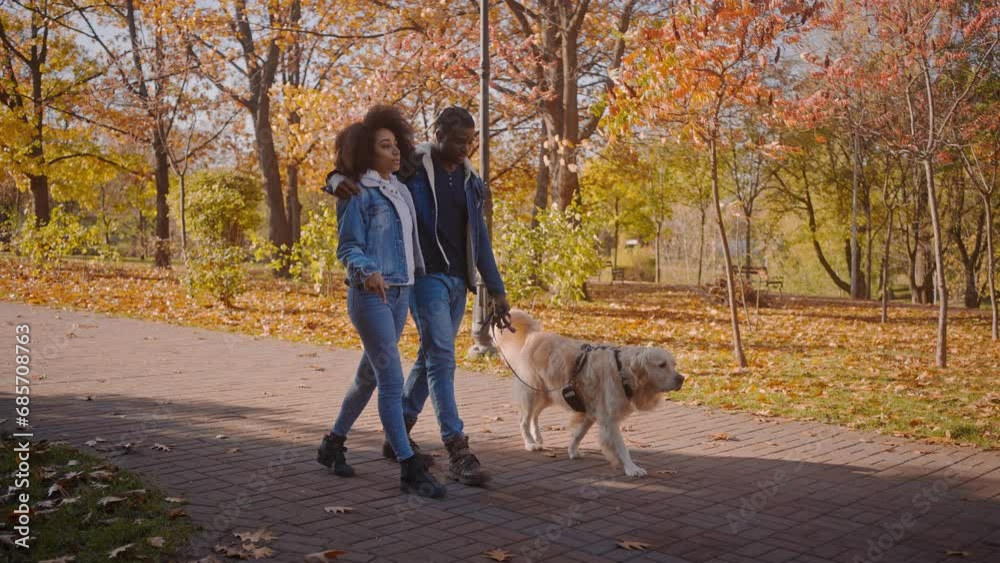 Happy African-American couple walks dog in autumn park Happy African-American couple walks dog in autumn park