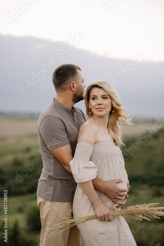 Portrait of a happy pregnant couple with a bouquet of sunflowers spending time together walking in the mountains at sunset