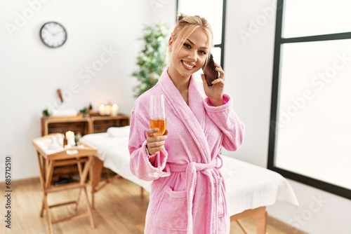 Young caucasian woman wearing bathrobe drinking champagne talking on smartphone at beauty salon