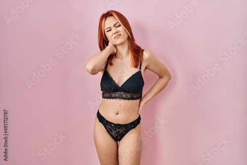 Young caucasian woman wearing lingerie over pink background suffering of neck ache injury, touching neck with hand, muscular pain