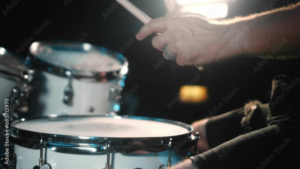The drummer plays drums in a dark studio with lights on the back.