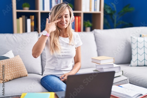 Young blonde woman studying using computer laptop at home pointing with hand finger to face and nose, smiling cheerful. beauty concept