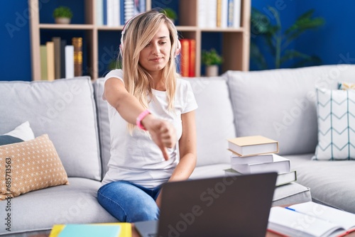 Young blonde woman studying using computer laptop at home looking unhappy and angry showing rejection and negative with thumbs down gesture. bad expression.