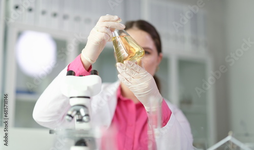Scientist chemist looking at flask with yellow brake oil in chemistry lab closeup. Quality control of petroleum products concept