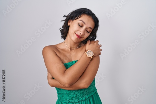 Young hispanic woman standing over isolated background hugging oneself happy and positive, smiling confident. self love and self care