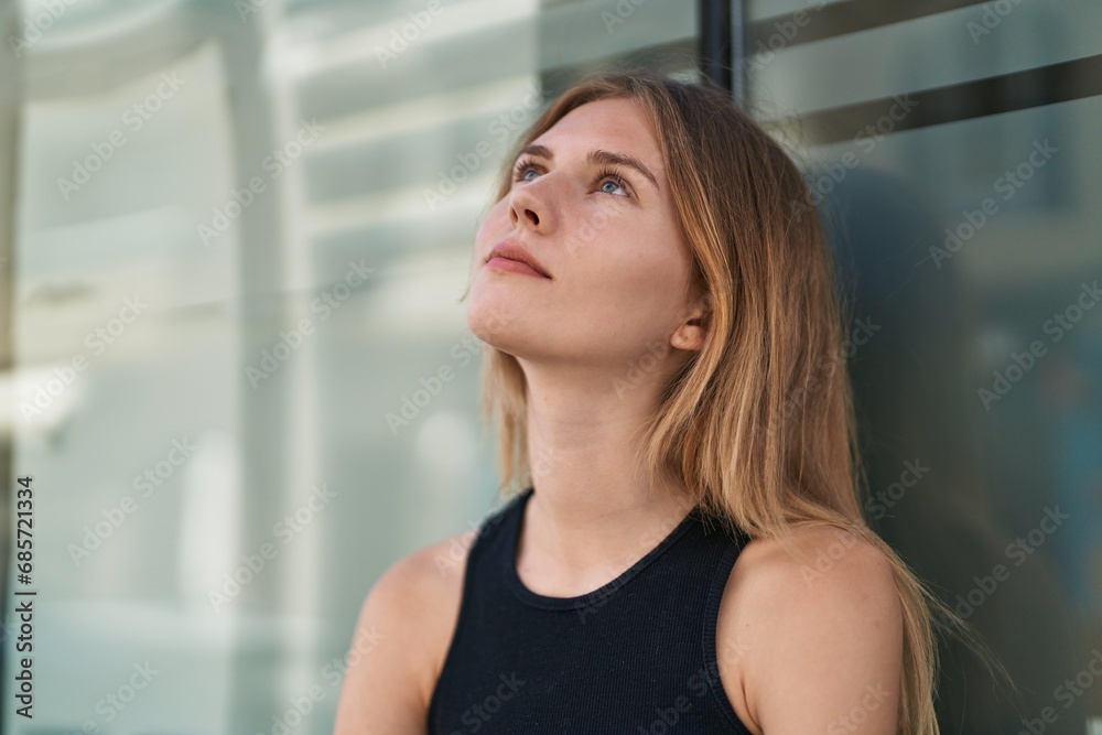 Young blonde woman looking to the sky with serious expression at street