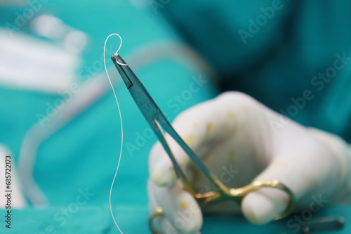 Doctor wearing white rubber gloves Hold the suture needle with pliers on the green cloth.