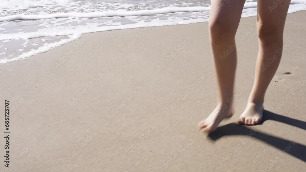 A girl walks along a sandy beach along the sea, leaving footprints. Close-up. Holidays at sea.