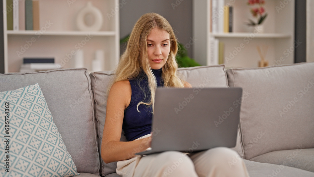 Young blonde woman using laptop sitting on sofa at home Young blonde woman using laptop sitting on sofa at home
