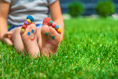 Child feet drawing smile in the park on the grass. Selective focus. © yanadjan