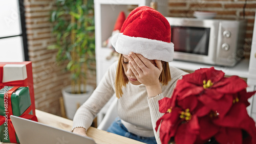 Billede på lærred Young blonde woman wearing christmas hat using laptop looking upset at coffee sh
