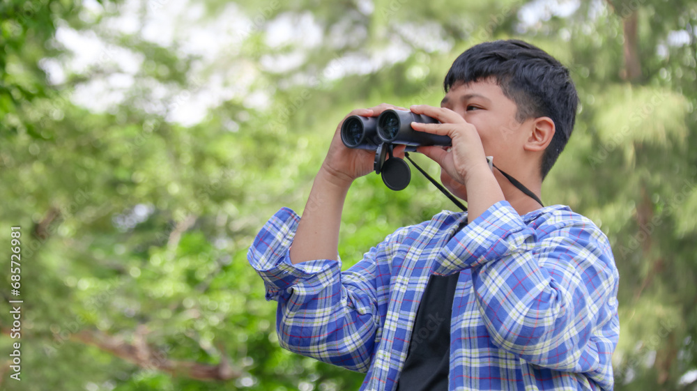 Young Asian boy is using a binocular to lookout for birds and animals in a local park, soft and selective focus Young Asian boy is using a binocular to lookout for birds and animals in a local park, soft and selective focus