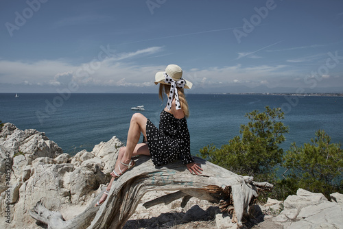 Young woman in straw hat sitting on edge of cliff and looking at sea. Salou, Costa Dorada in province of Tarragona. Spain.