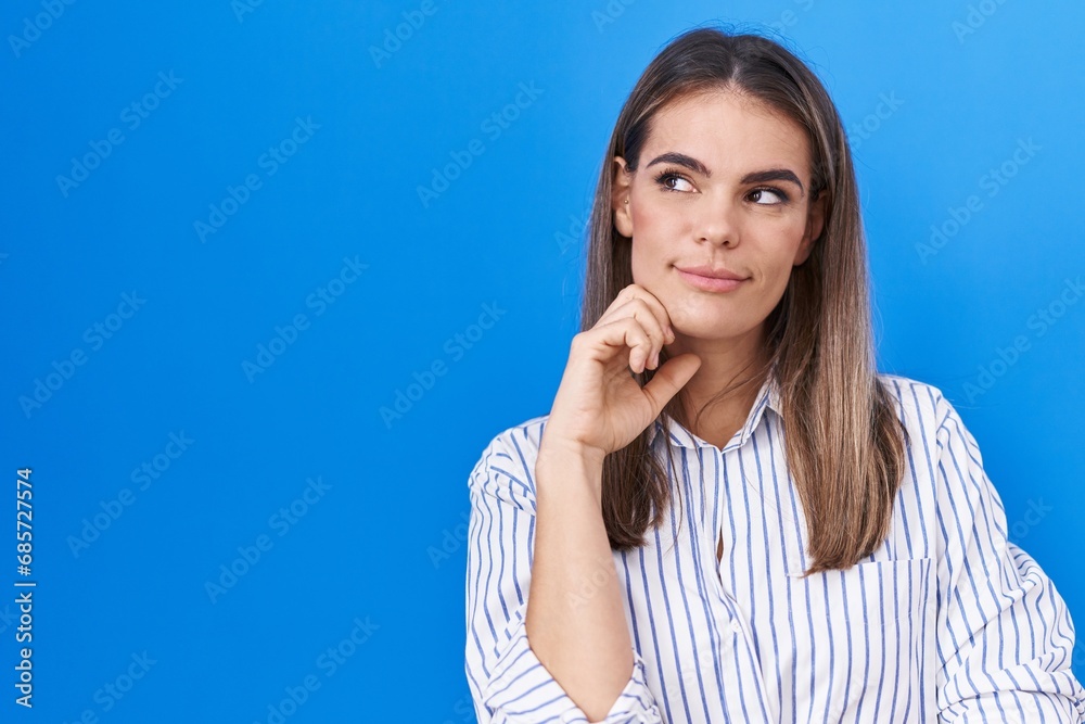 Hispanic young woman standing over blue background with hand on chin thinking about question, pensive expression. smiling with thoughtful face. doubt concept. Hispanic young woman standing over blue background with hand on chin thinking about question, pensive expression. smiling with thoughtful face. doubt concept.