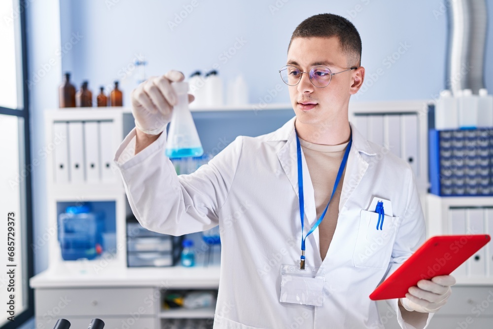 Young hispanic man scientist measuring liquid using touchpad at laboratory Young hispanic man scientist measuring liquid using touchpad at laboratory