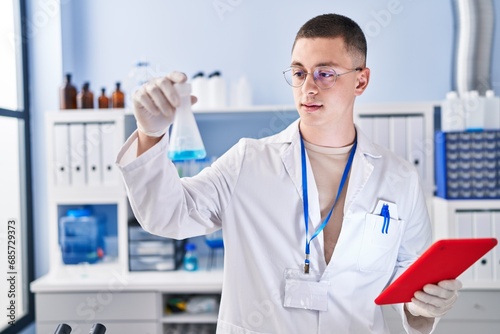 Young hispanic man scientist measuring liquid using touchpad at laboratory