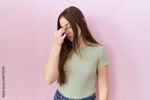 Beautiful brunette woman standing over pink background tired rubbing nose and eyes feeling fatigue and headache. stress and frustration concept.