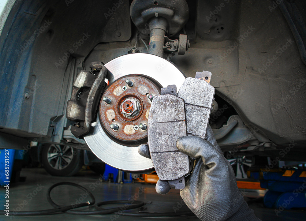 Used car brake pads in the hands of a mechanic with brake discs and brake calipers on the background , Car spare parts and maintenance concept - obrazy, fototapety, plakaty 