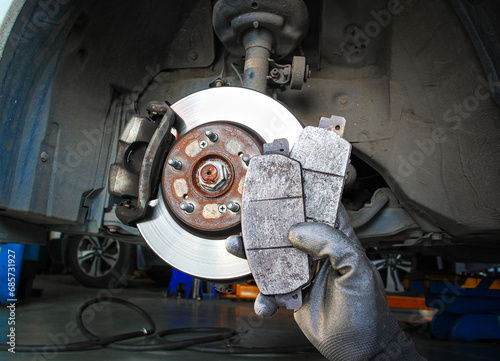 Used car brake pads in the hands of a mechanic with brake discs and brake calipers on the background , Car spare parts and maintenance concept photo