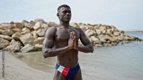 African american man tourist standing shirtless training yoga at the beach