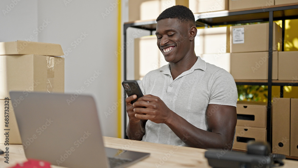 African american man ecommerce business worker using smartphone and laptop smiling at office