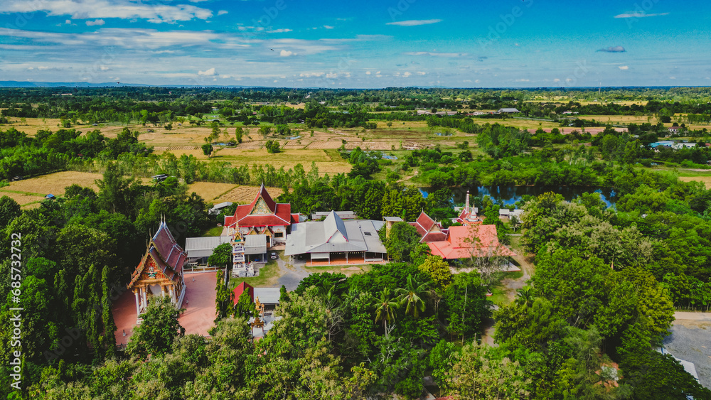 High angle photo, taken with a drone, landscape of the Thai temple area, surrounded by trees, bright sky, lots of sunshine.