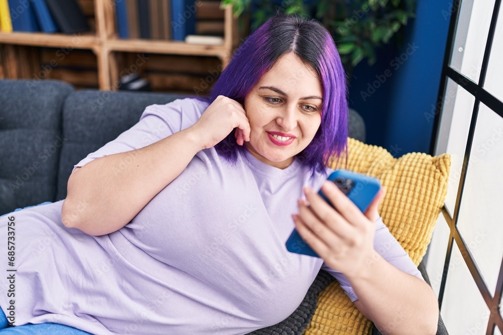 Young beautiful plus size woman using smartphone lying on sofa at home Young beautiful plus size woman using smartphone lying on sofa at home