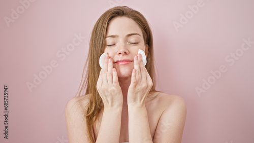 Young blonde woman smiling confident cleaning face with cotton pads over isolated pink background