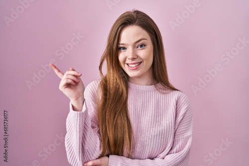 Young caucasian woman standing over pink background with a big smile on face, pointing with hand finger to the side looking at the camera. © Krakenimages.com
