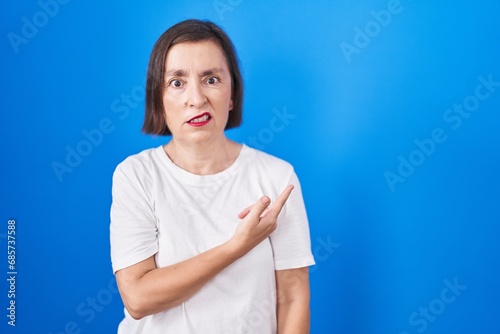 Middle age hispanic woman standing over blue background pointing aside worried and nervous with forefinger, concerned and surprised expression © Krakenimages.com