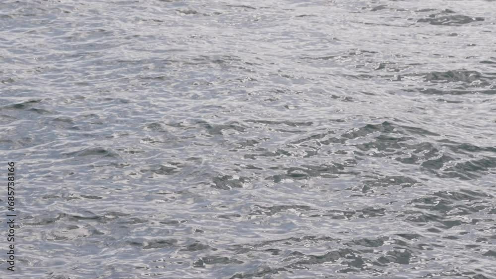 Bright light shines on slowly moving waves in ocean water near coast Bright light shines on slowly moving waves in ocean water near coast