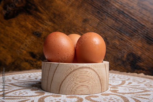 eggs, three eggs placed on a circular wooden container, at the base you can see a mat with mandalas and the bottom is made of wood