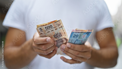 Young hispanic man counting mexican pesos at street photo