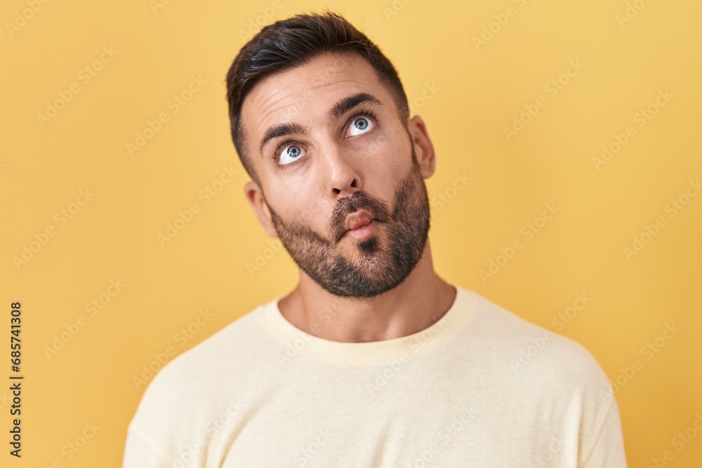 Fototapeta premium Handsome hispanic man standing over yellow background making fish face with lips, crazy and comical gesture. funny expression.