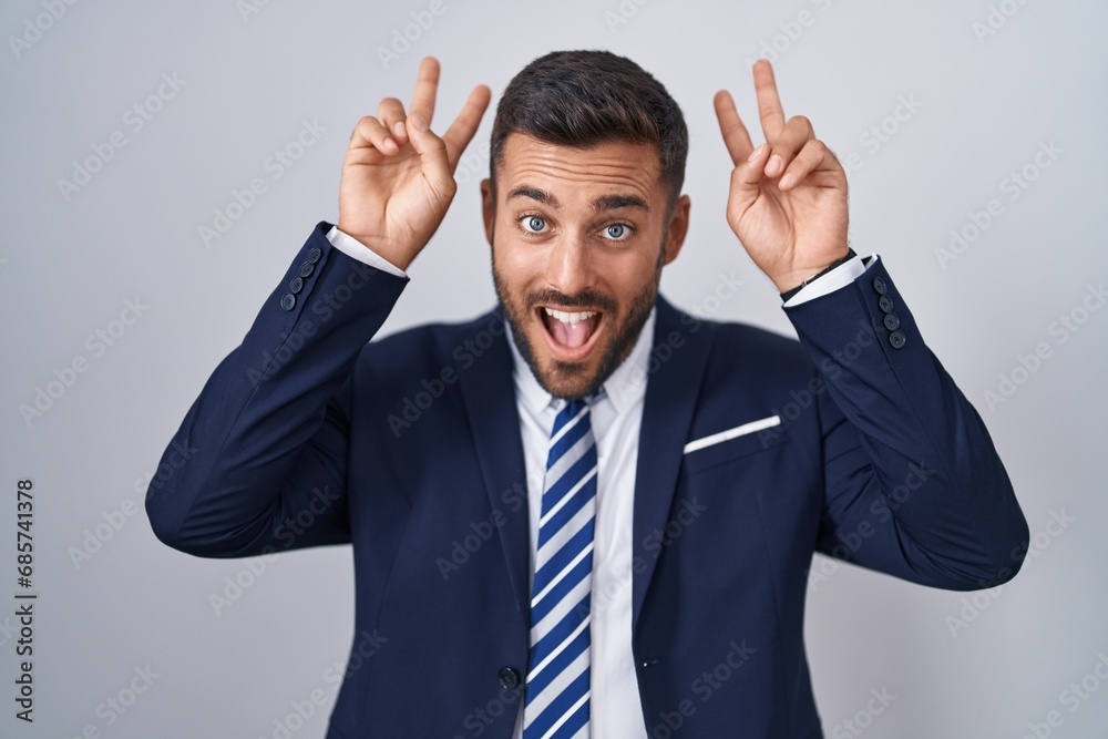 Handsome hispanic man wearing suit and tie posing funny and crazy with fingers on head as bunny ears, smiling cheerful Handsome hispanic man wearing suit and tie posing funny and crazy with fingers on head as bunny ears, smiling cheerful