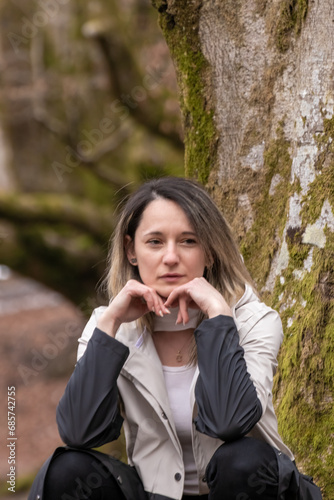 a woman is sitting against a tree, their hands forming a heart shape, in a forest setting