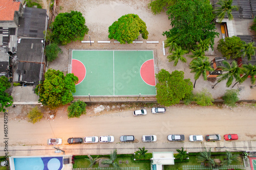 A Street with some parked cars and a small tennis training court seen from above