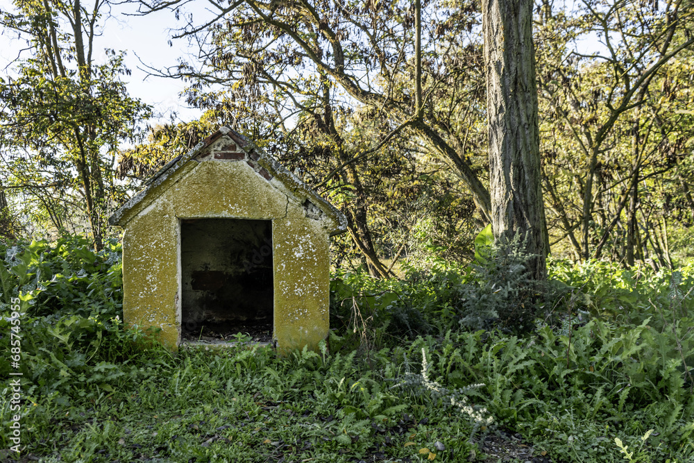 A cement doghouse outside surrounded by trees and abundant grass A cement doghouse outside surrounded by trees and abundant grass