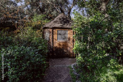 A small wooden storage cabin at the end of a path surrounded by hedges and vegetation © Toyakisfoto.photos